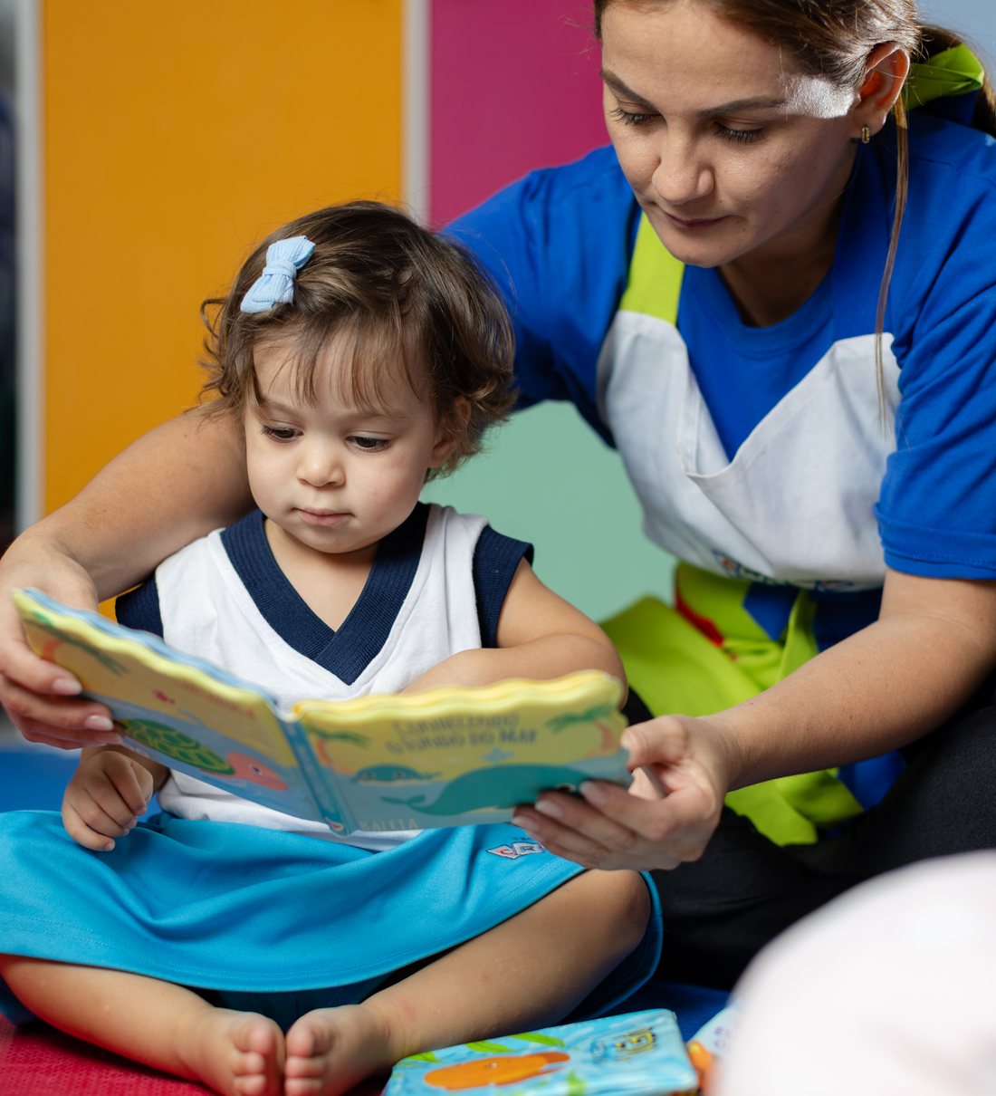 Educadora da Criar Baby lendo um livro com um aprendiz no colo