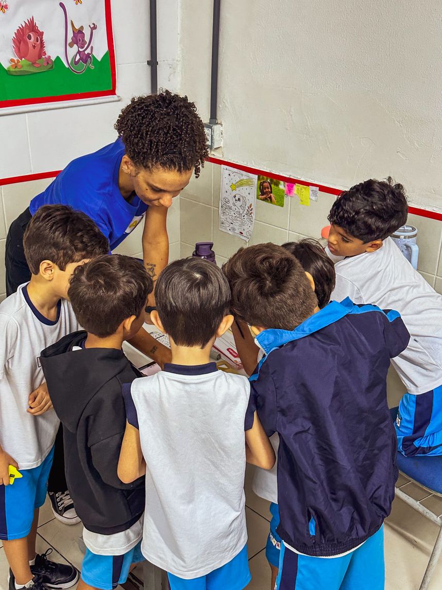 Educadora agachada na altura das crianças durante atividade em grupo