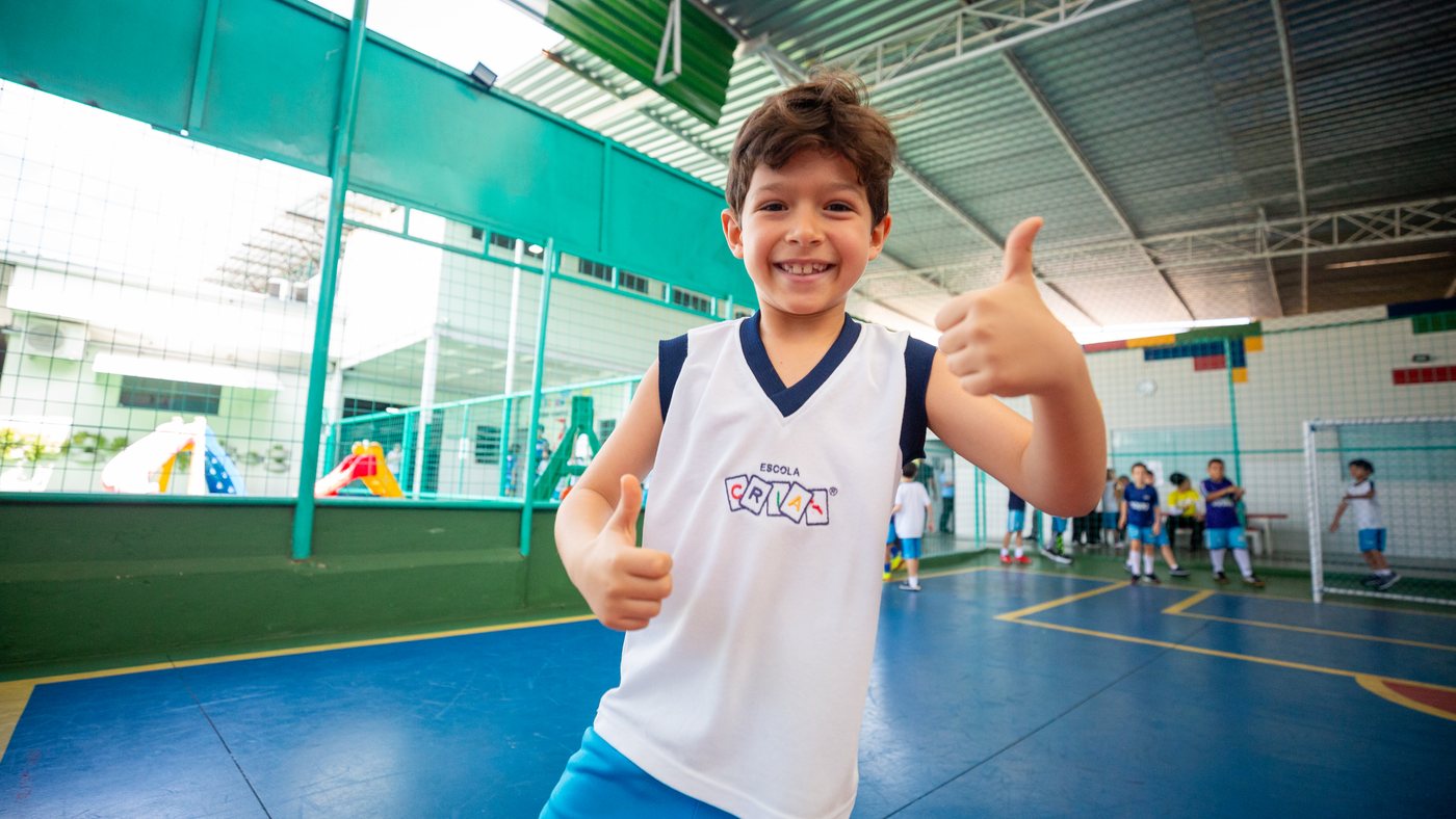Aluno da Escola Criar faz sinal de positivo na quadra da escola