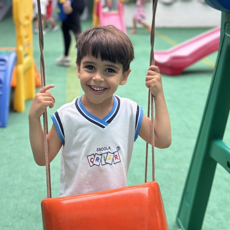 Aluno da Escola Criar sorri no balanço do parquinho